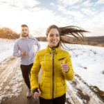 Athletic couple running together on a winter road, demonstrating persistence and focus on fitness goals during the colder season.