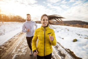 Athletic couple running together on a winter road, demonstrating persistence and focus on fitness goals during the colder season.