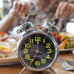 Alarm clock in front of a man, signaling the end of his intermittent fasting period, allowing him to enjoy a healthy meal as part of his weight loss plan.