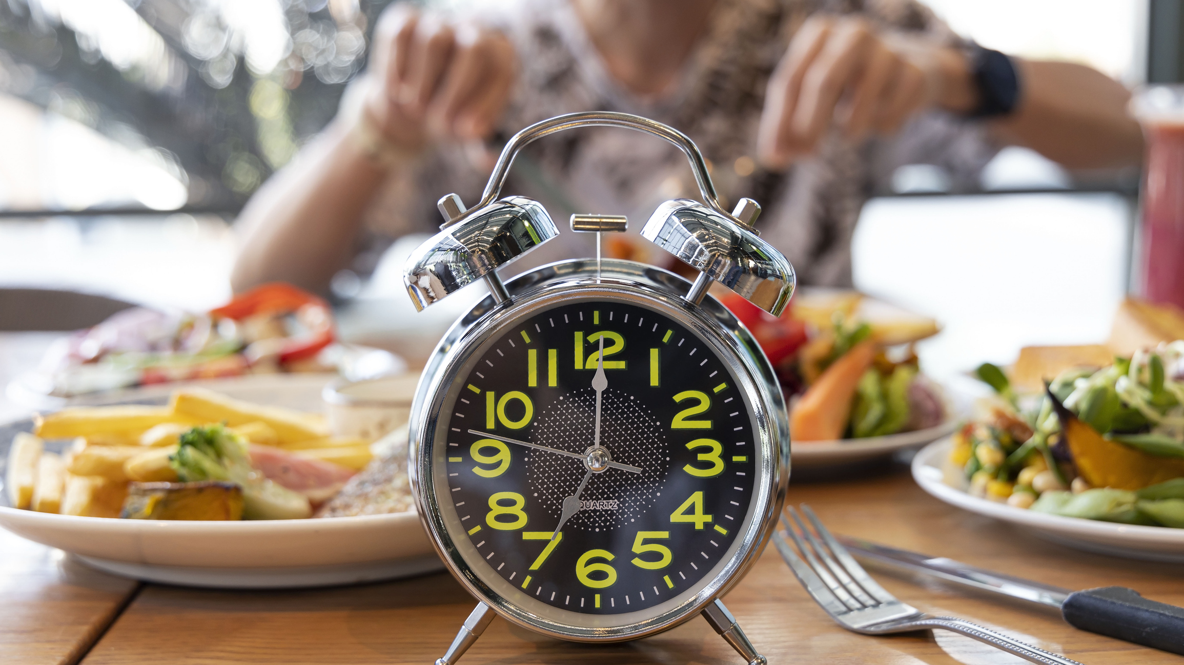 Alarm clock in front of a man, signaling the end of his intermittent fasting period, allowing him to enjoy a healthy meal as part of his weight loss plan.