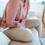 A woman sitting on the couch, visibly uncomfortable, reflecting the painful symptoms of a urinary tract infection (UTI).