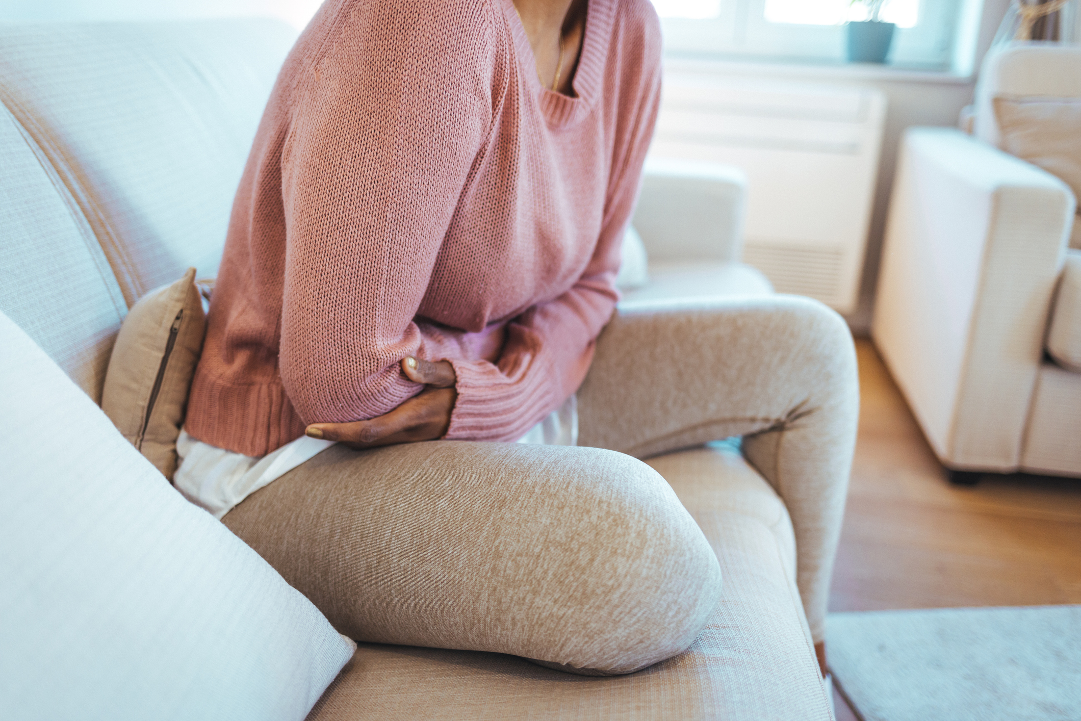 A woman sitting on the couch, visibly uncomfortable, reflecting the painful symptoms of a urinary tract infection (UTI).