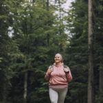 A plus-size woman hiking through a forest, highlighting the importance of prioritizing exercise in the journey towards long-term weight management.