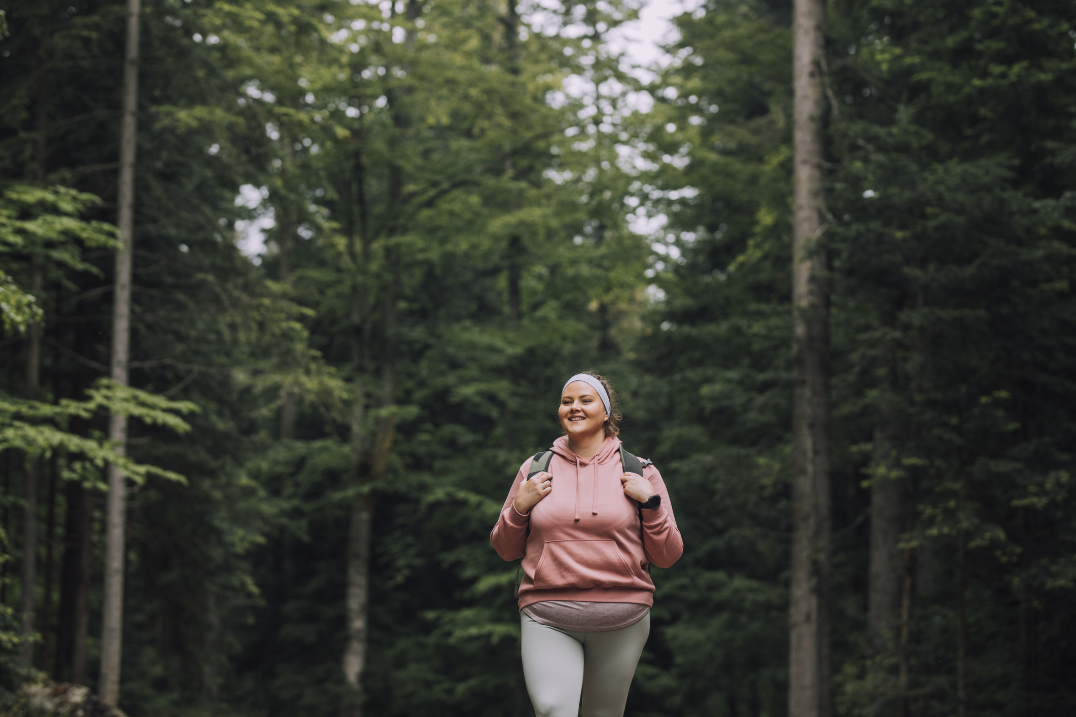 A plus-size woman hiking through a forest, highlighting the importance of prioritizing exercise in the journey towards long-term weight management.