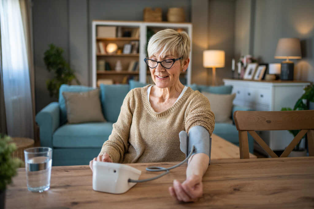 A woman measuring her blood pressure at home, symbolizing the importance of regular monitoring in managing blood pressure and choosing the right medication for heart health