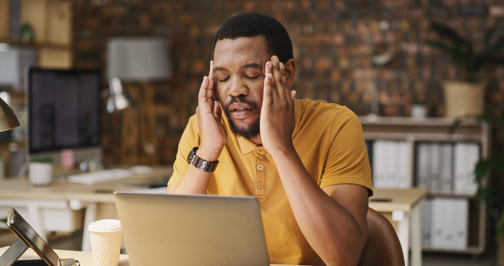 A man sitting at his laptop, stressed and anxious, illustrating some of the side effects of discontinuing Prozac® (fluoxetine), such as anxiety and emotional strain.